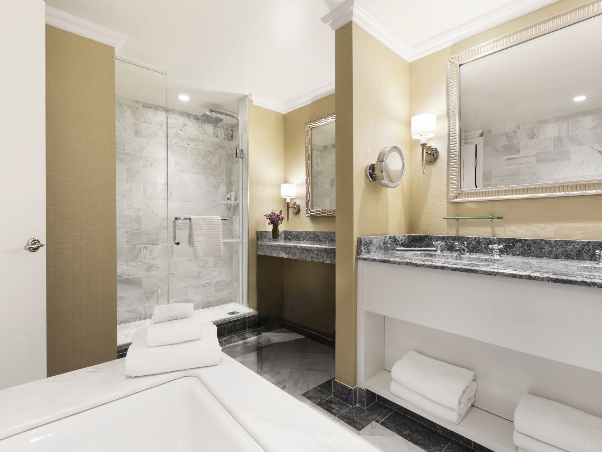 This image shows a modern bathroom with a bathtub, double sink vanity, large mirror, and glass-enclosed shower area with neatly folded towels.