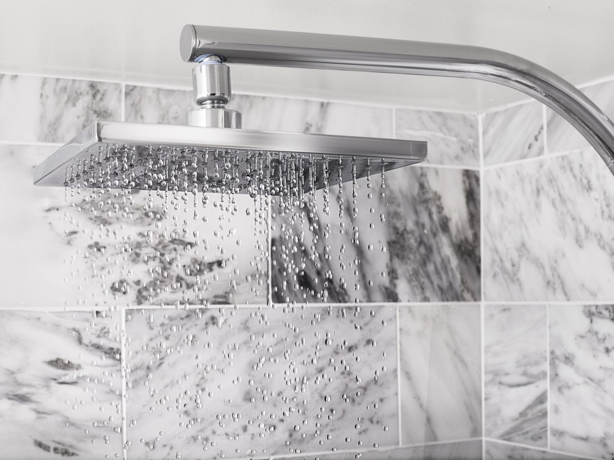 Modern shower head with water flowing, against a marble tile backdrop.