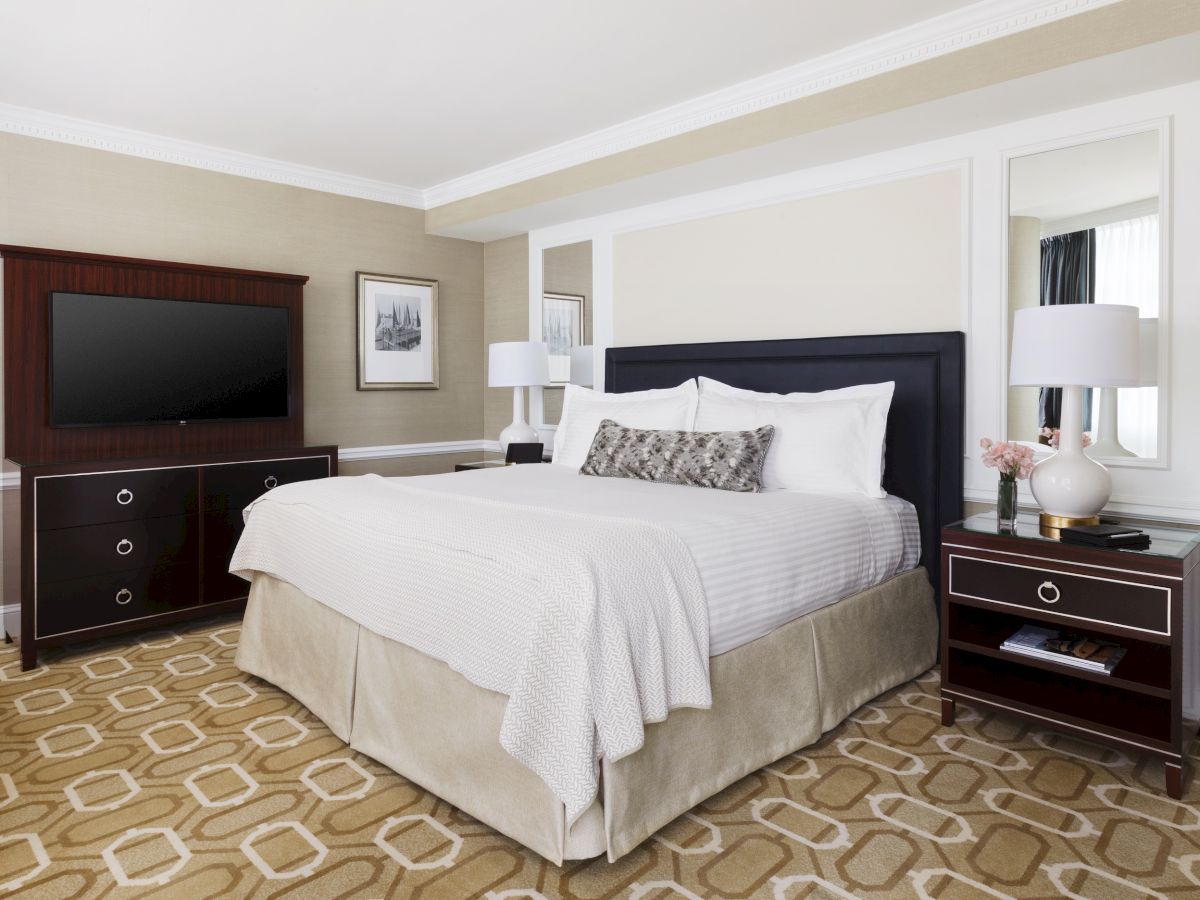 A neatly made bed in a well-decorated room with furniture and a TV.