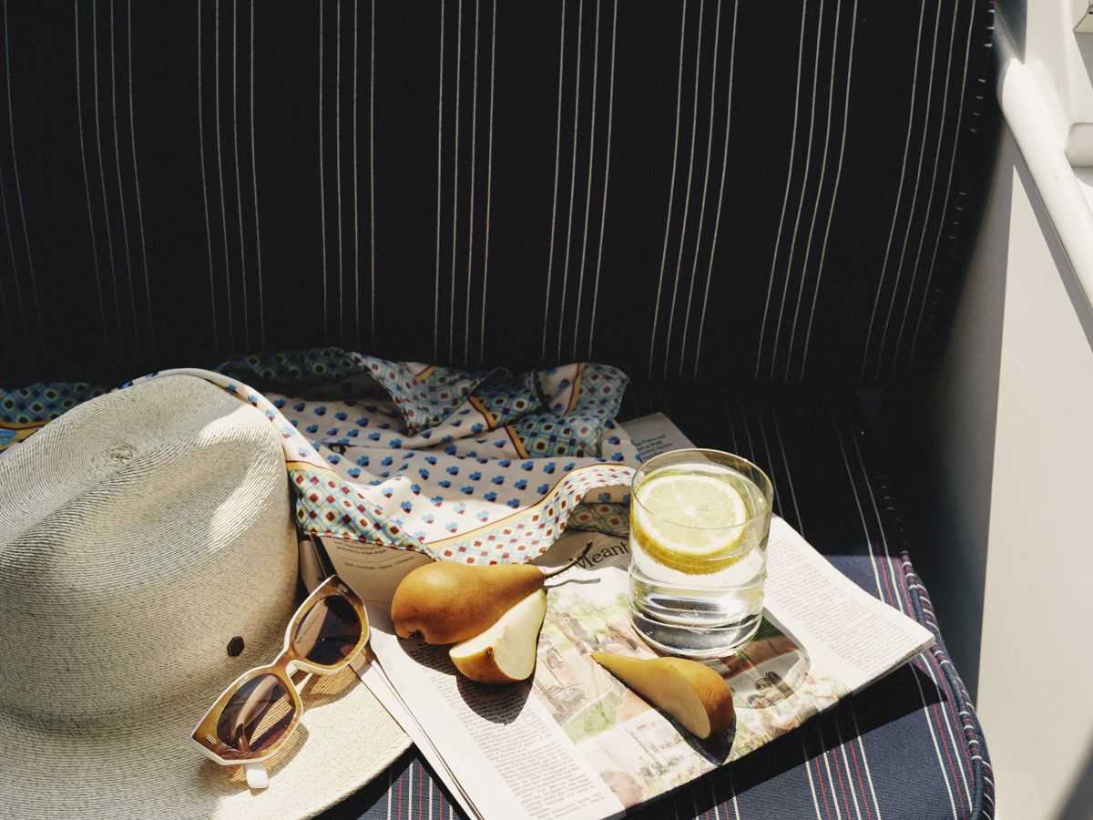 Boat seat with a straw hat, sunglasses, kiwi, and drink.