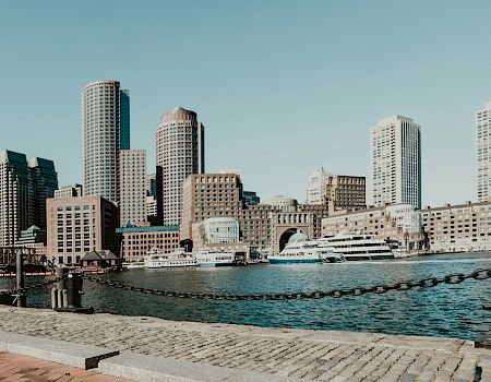 City skyline, buildings, clear sky, waterfront, and boat visible.