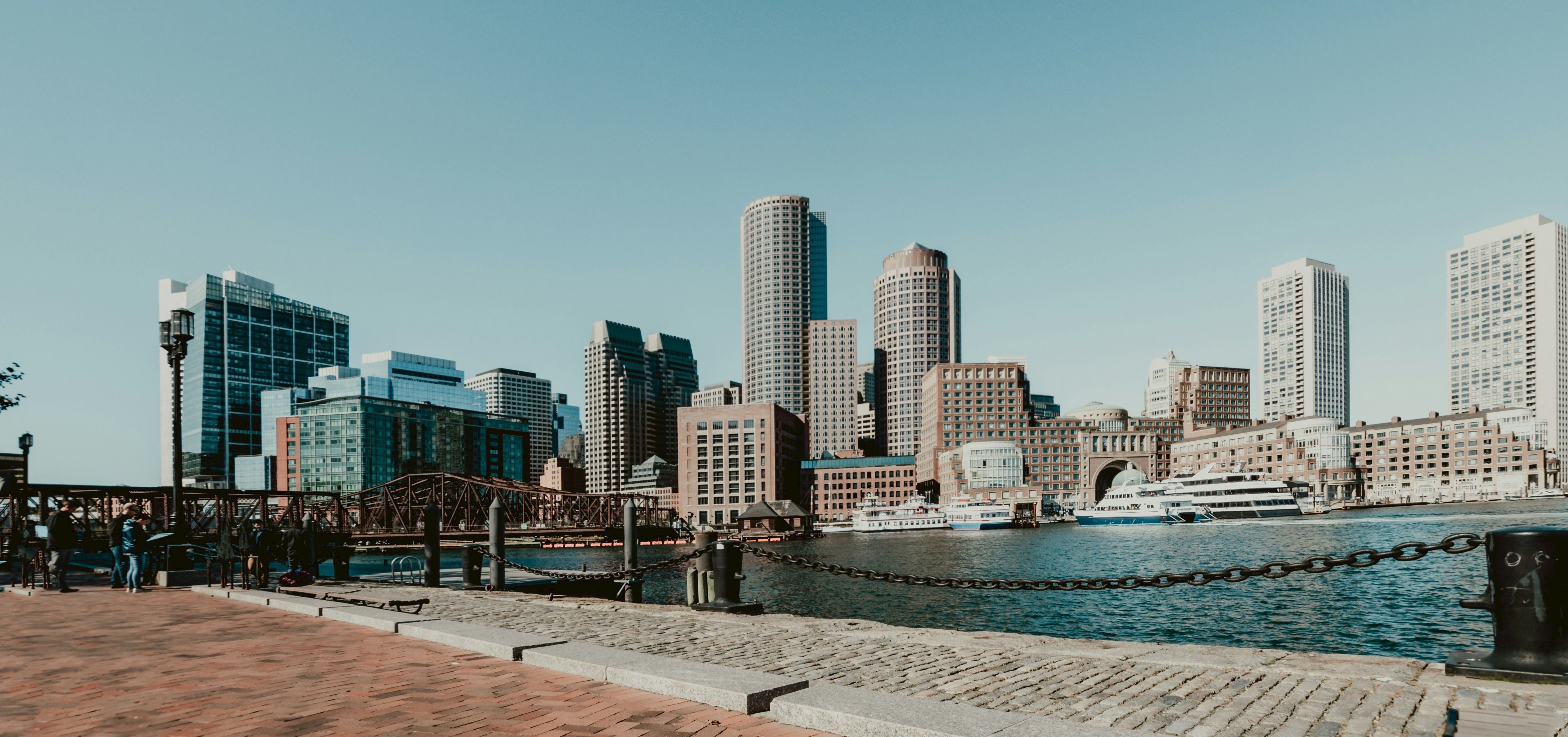 City skyline, buildings, clear sky, waterfront, and boat visible.