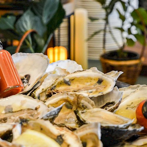 An assortment of oysters on a platter, adorned with lemon slices, and accompanied by two dropper bottles containing a red liquid.