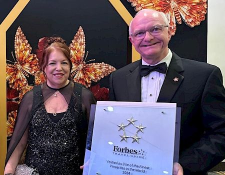 Two people are smiling, holding a Forbes certificate.