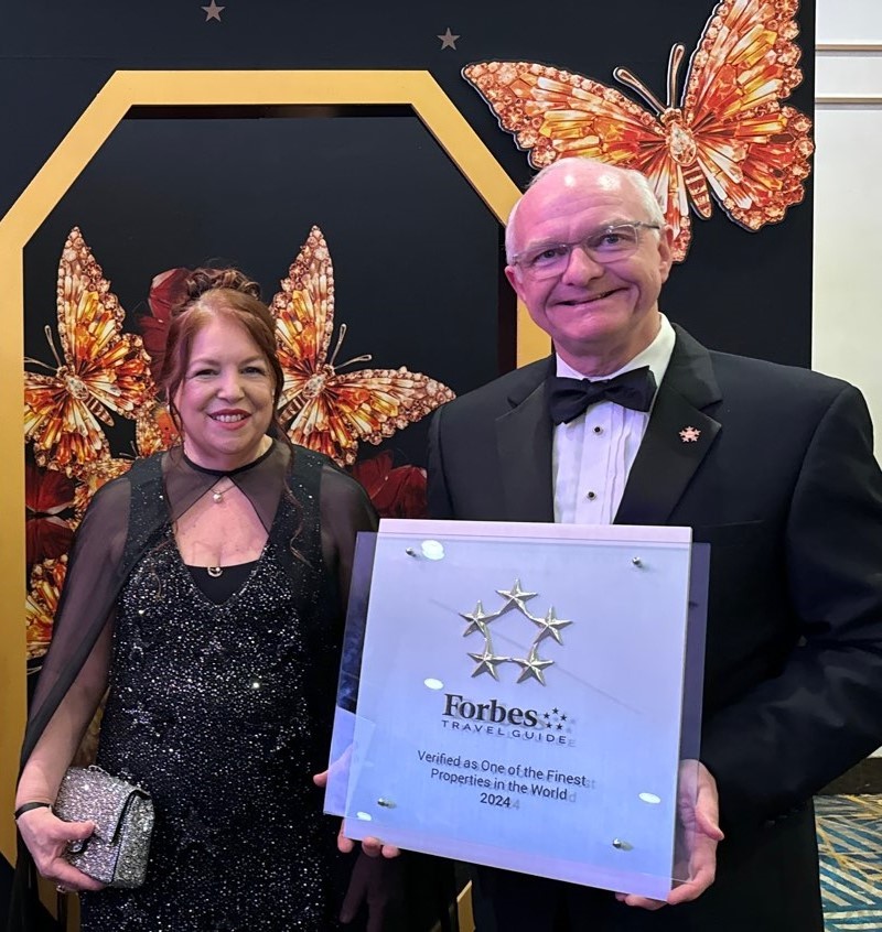 Two people are smiling, holding a Forbes certificate.