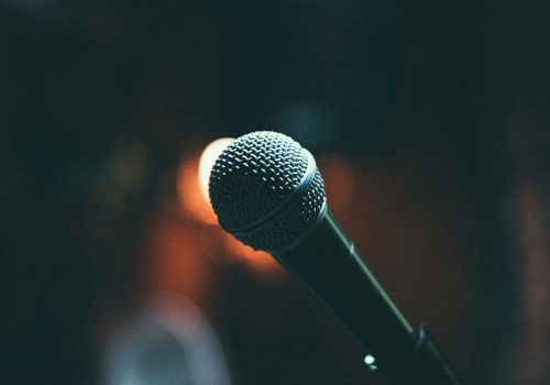 A close-up shot of a microphone in a dark setting with a blurred background featuring warm lights.