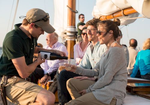 A person is pouring a drink for a woman on a boat with several people enjoying the setting.