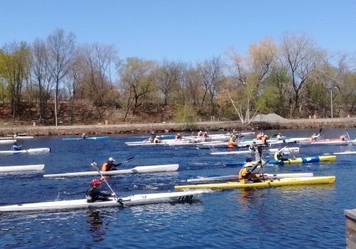 People are kayaking and canoeing in a river, surrounded by trees on a clear day.