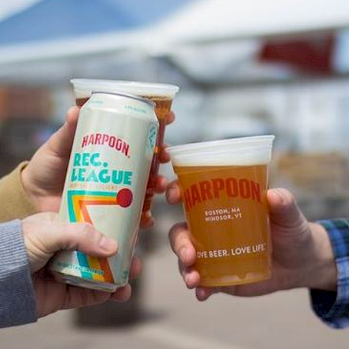 Three hands are holding beer: one holding a can and two holding plastic cups, all branded 