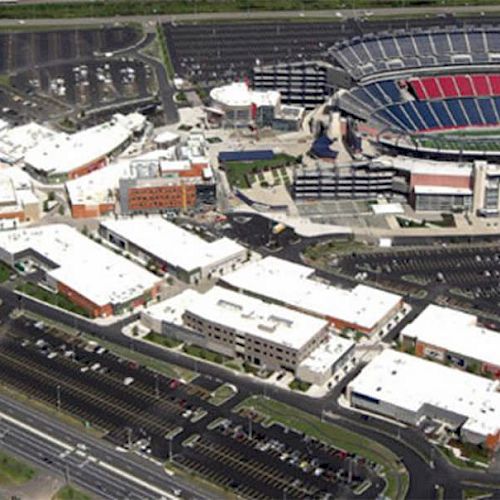 An aerial view of a large event stadium surrounded by numerous buildings and extensive parking lots, with major roads visible in the foreground.