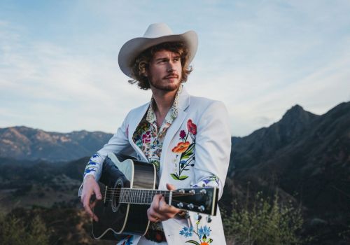 Yung Gravy holding a Guitar wearing White Suit