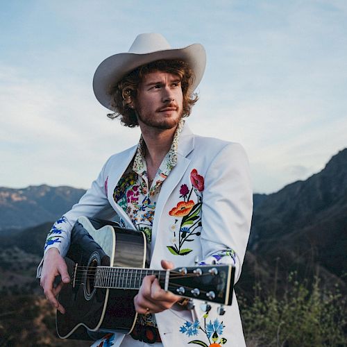 Yung Gravy holding a Guitar wearing White Suit