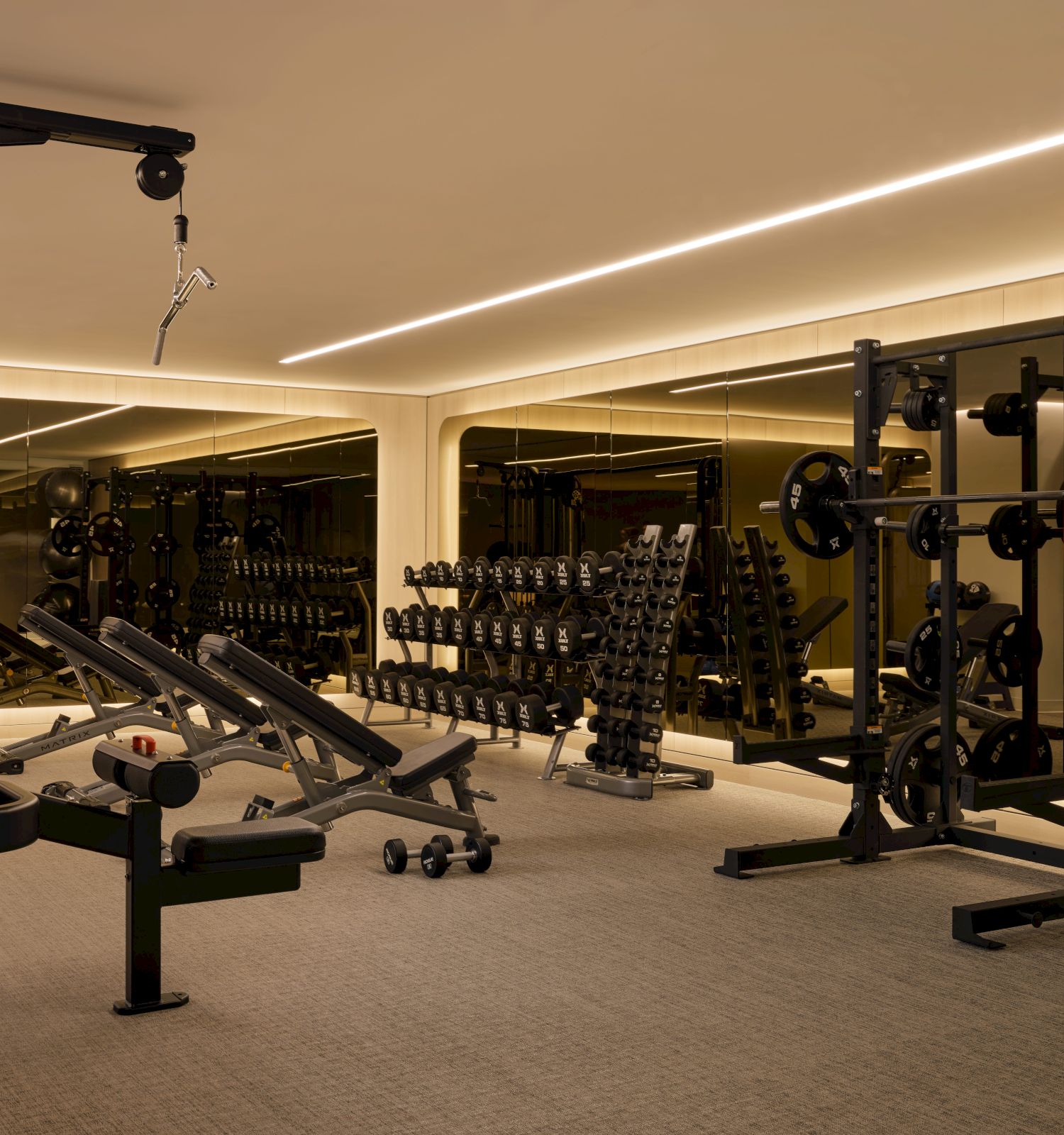 A gym with equipment like weight racks, benches, and mirrors. The space is well-lit with a modern design and spacious layout.