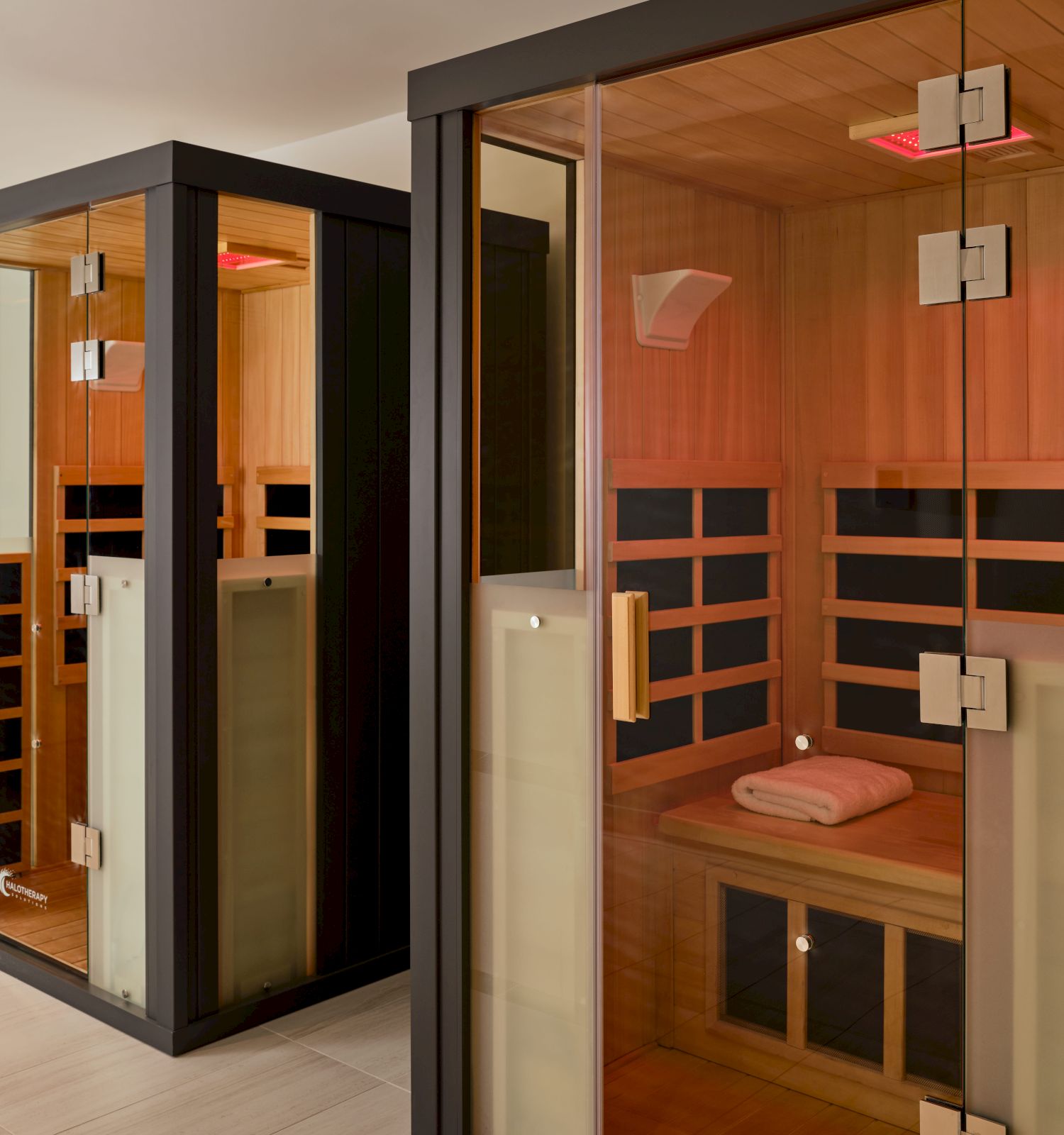 The image shows two modern infrared saunas with glass doors and wooden interiors, located indoors.