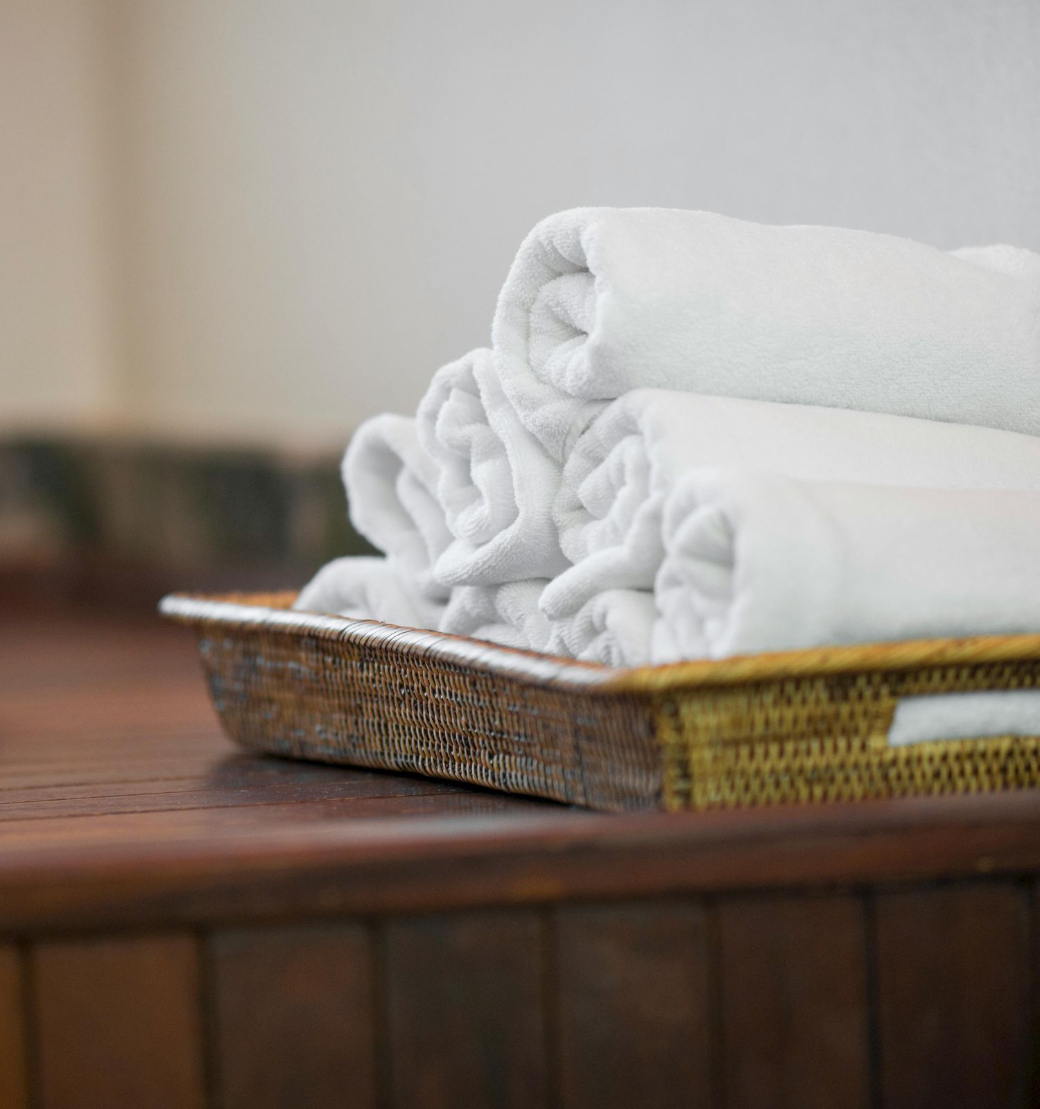 The image shows a wicker basket holding neatly rolled white towels on a wooden counter, next to a sink.