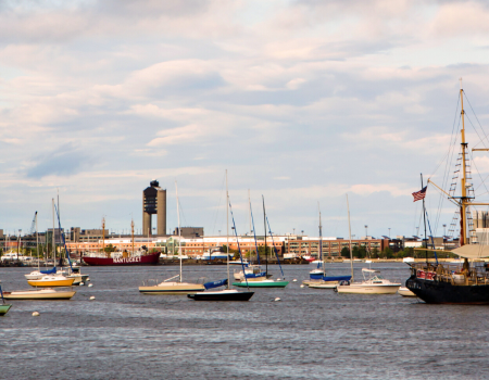 The image shows a harbor with various boats and ships docked, under a sky with some cloud cover.