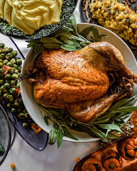 A bountiful Thanksgiving meal with a roasted turkey, mashed potatoes, stuffing, Brussels sprouts, sweet potatoes, and decorative pumpkins.