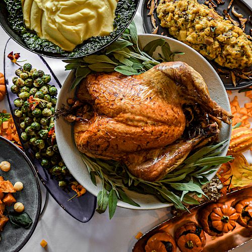 A bountiful Thanksgiving meal with a roasted turkey, mashed potatoes, stuffing, Brussels sprouts, sweet potatoes, and decorative pumpkins.