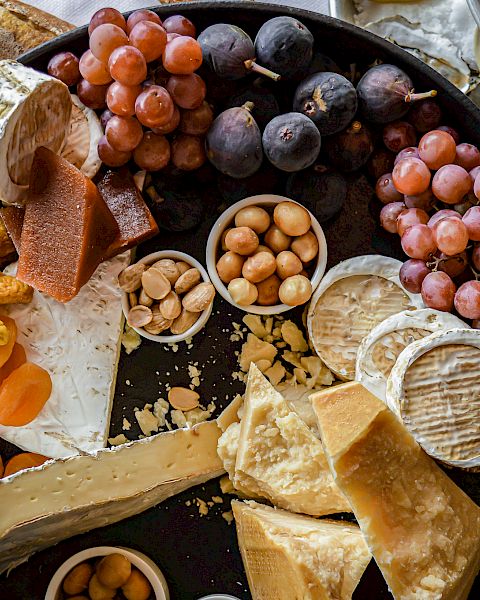 A charcuterie board featuring various cheeses, grapes, dried fruits, nuts, and bread, with oysters and lemon in the background.