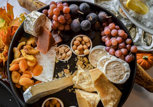 A charcuterie board featuring various cheeses, grapes, dried fruits, nuts, and bread, with oysters and lemon in the background.