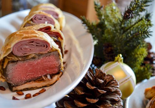 A sliced beef Wellington dish served on a white plate, with holiday decorations including pinecones and ornaments in the background.