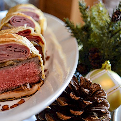 A sliced beef Wellington dish served on a white plate, with holiday decorations including pinecones and ornaments in the background.