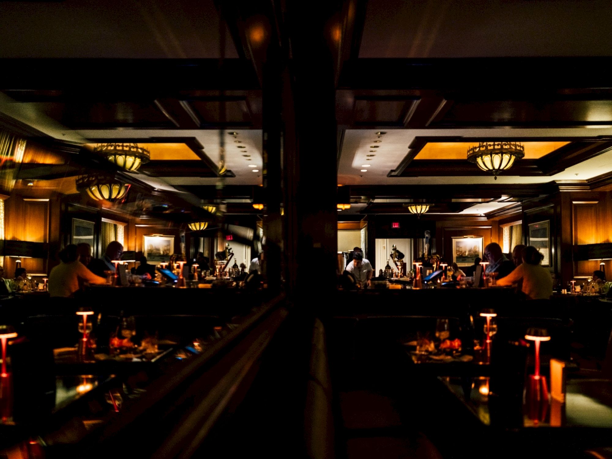 The image shows a dimly lit restaurant interior with elegant lighting, mirrors, and people dining, creating a cozy, sophisticated ambiance.