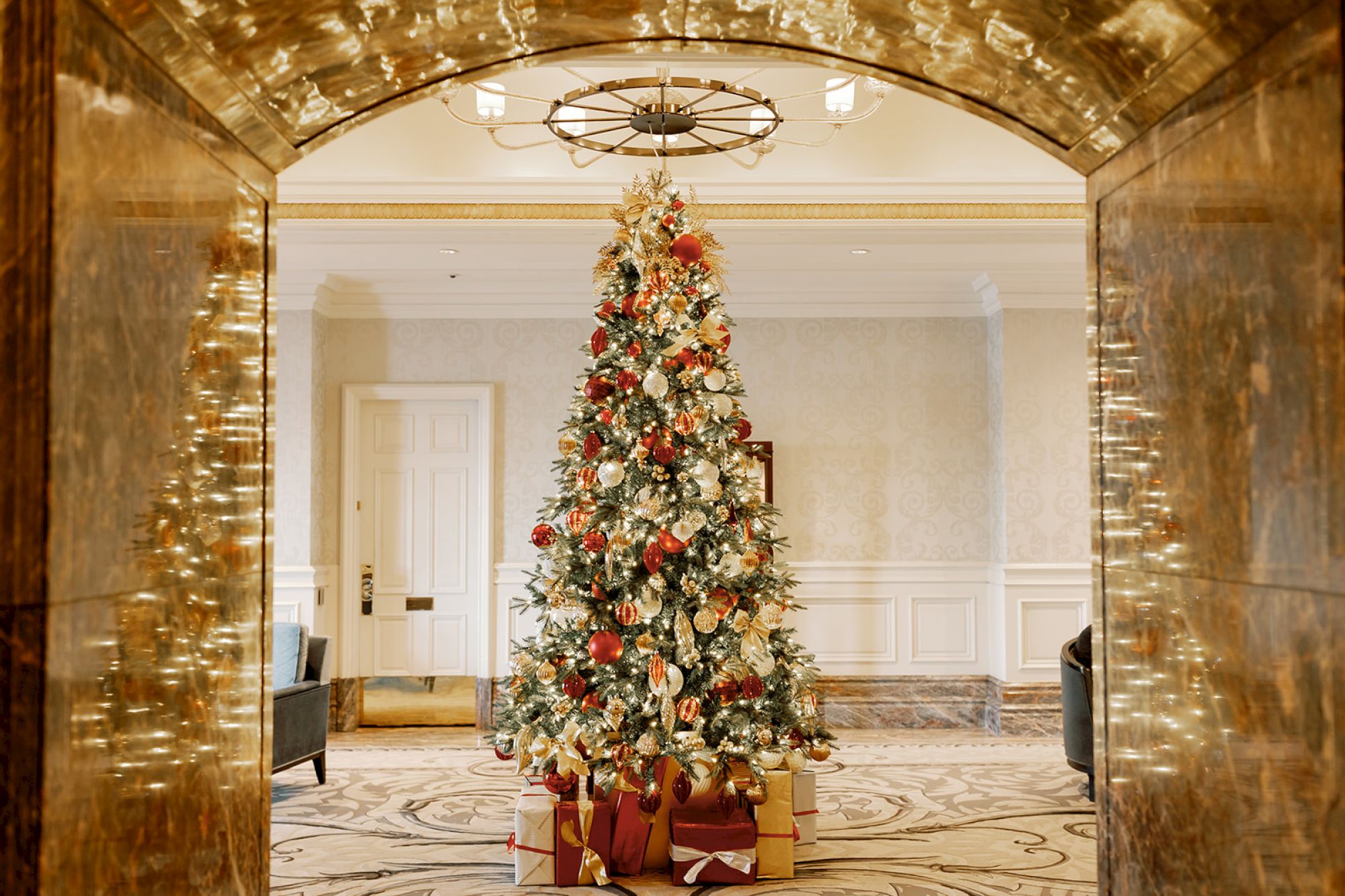 A decorated Christmas tree with ornaments and gifts underneath, set in an elegantly furnished room with marble accents.