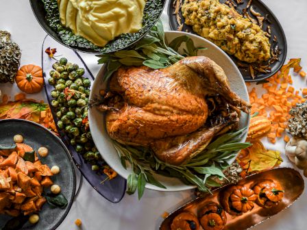 A Thanksgiving dinner spread featuring a roasted turkey, mashed potatoes, stuffing, Brussels sprouts, sweet potatoes, and decorative pumpkins.