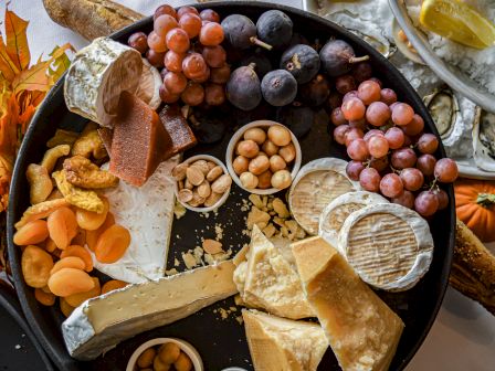 A charcuterie board with various cheeses, grapes, nuts, dried apricots, crackers, and a background of oysters and lemon.