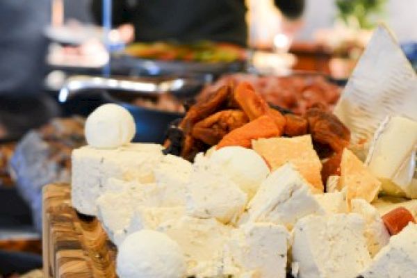 The image shows a cheese platter with assorted cheeses and dried fruits, displayed on a wooden board at a buffet or gathering.