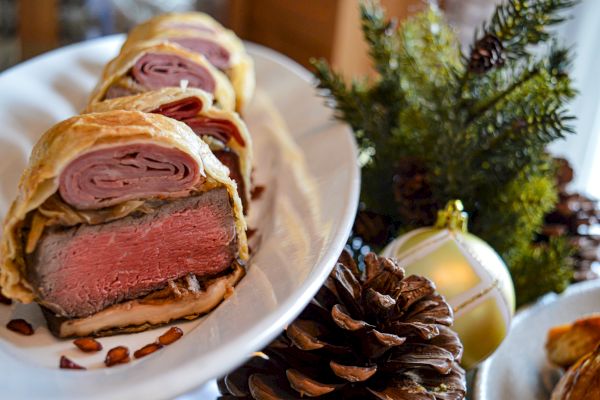 Sliced beef Wellington on a plate with holiday decorations, pinecones, and greenery, creating a festive and appetizing display.