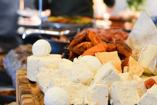 An assortment of cheeses on a wooden board, accompanied by dried fruits, displayed on a table in a buffet setting.