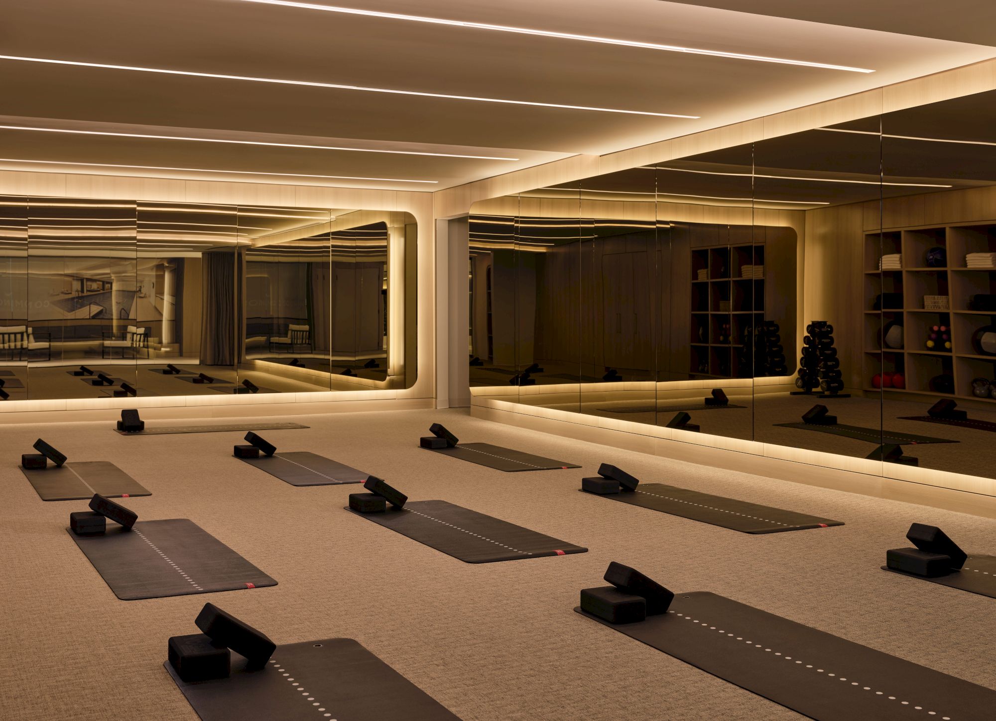 A modern yoga studio with yoga mats and blocks laid out on the floor, large mirrors on the wall, and soft lighting illuminating the space.