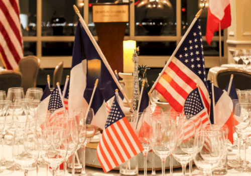 The image shows a table centerpiece with American and French flags, surrounded by empty glasses, set in a formal dining setting.