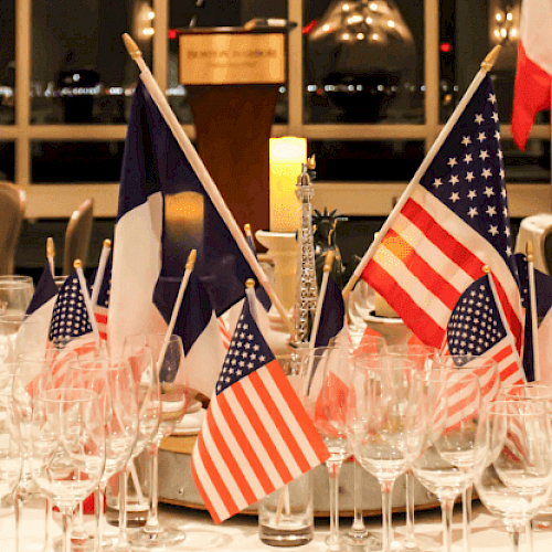 The image shows a table centerpiece with American and French flags, surrounded by empty glasses, set in a formal dining setting.