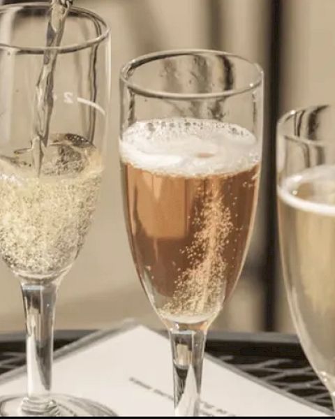 Three champagne flutes filled with sparkling beverages are placed on a table, with one being poured.