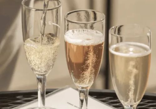 Three champagne flutes filled with sparkling beverages are placed on a table, with one being poured.