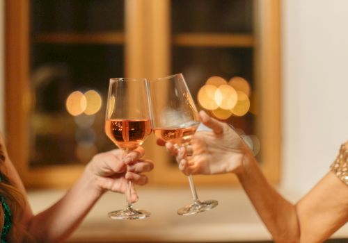 Two people clinking glasses of rosé wine in a warmly lit setting, with blurred lights in the background creating a festive atmosphere.