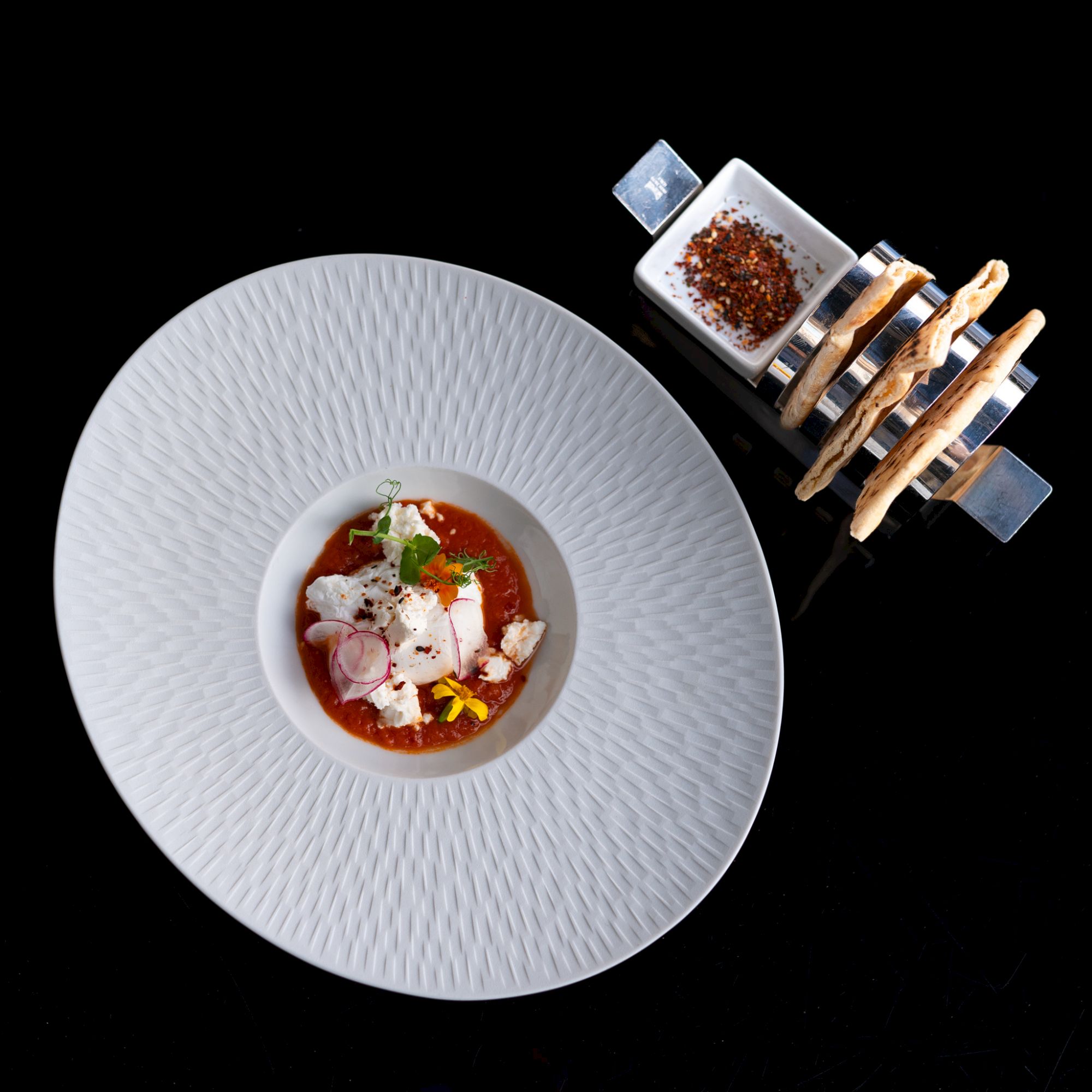 A bowl of soup with garnishes on a textured plate and bread.