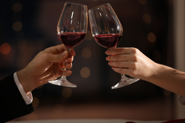 Two people clinking wine glasses during a candlelit dinner.