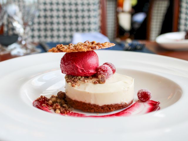 A dessert with a creamy base, topped with red sorbet, berries, and a crunchy wafer on a white plate.