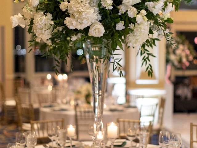 A elegantly set table with a tall floral centerpiece, white flowers, gold chairs, place settings, and a small table number 5 sign is pictured.