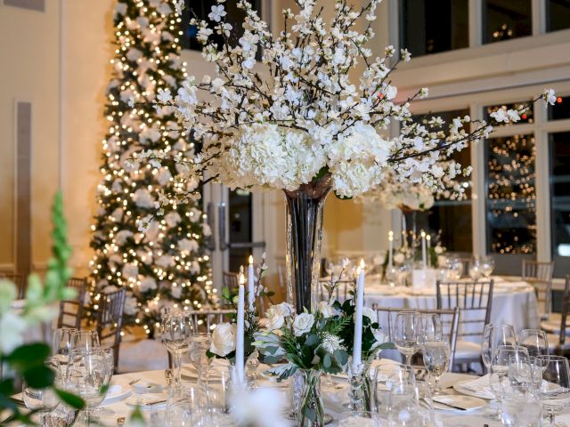 The image shows an elegantly decorated dining area with a large floral centerpiece, set tables, and a lit-up Christmas tree in the background.