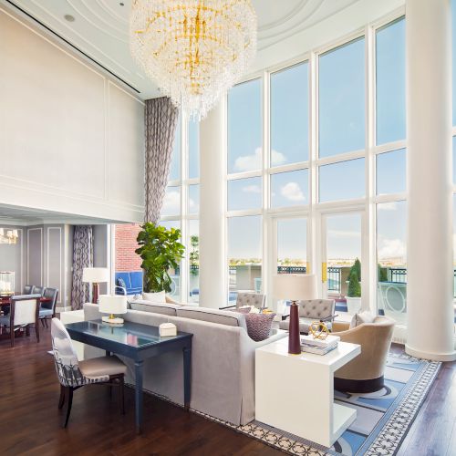 A luxurious living and dining area with large windows, elegant chandeliers, and modern furniture overlooking a balcony.