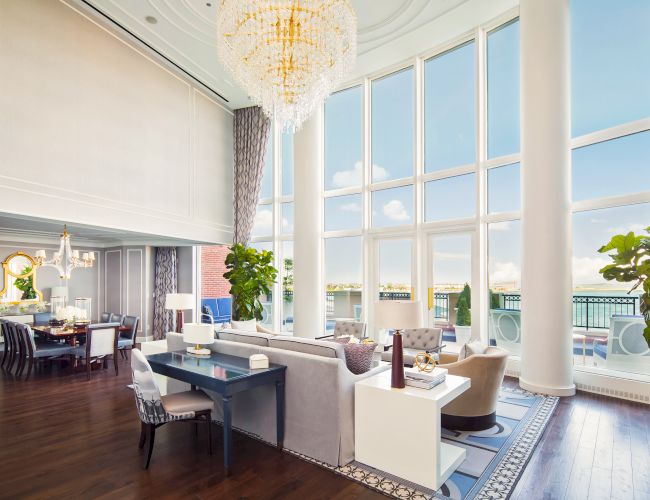 A luxurious living and dining area with large windows, elegant chandeliers, and modern furniture overlooking a balcony.