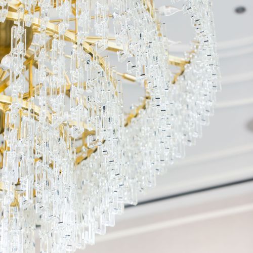 The image shows a luxurious chandelier with intricate crystal designs and a gold frame, suspended from a ceiling.