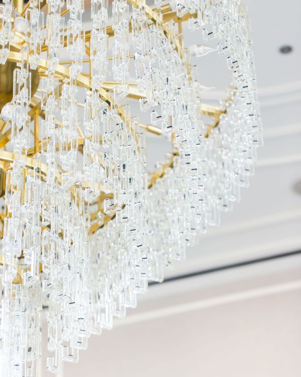 The image shows a luxurious chandelier with intricate crystal designs and a gold frame, suspended from a ceiling.