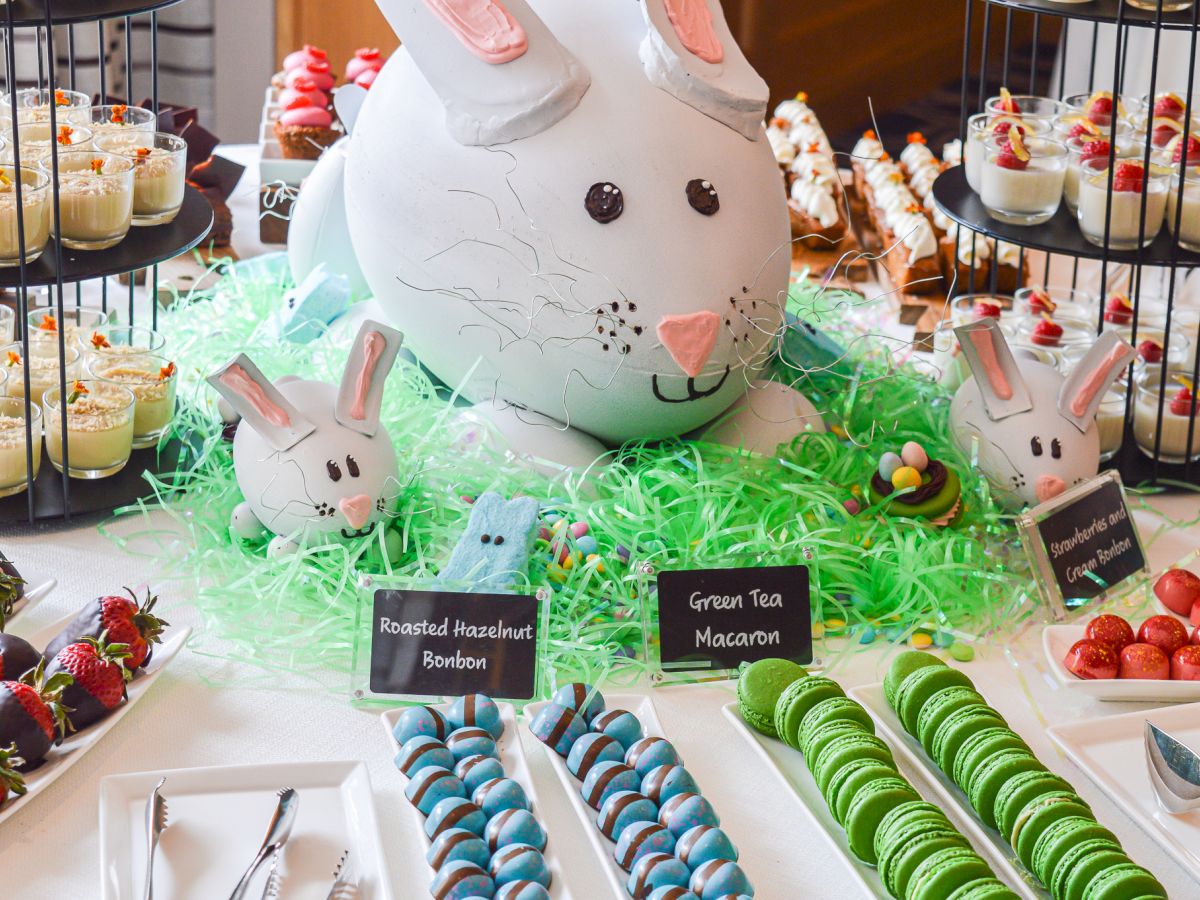 Dessert table with bunny decorations, green tea macarons, strawberries, bonbons, and assorted desserts, presented festively.