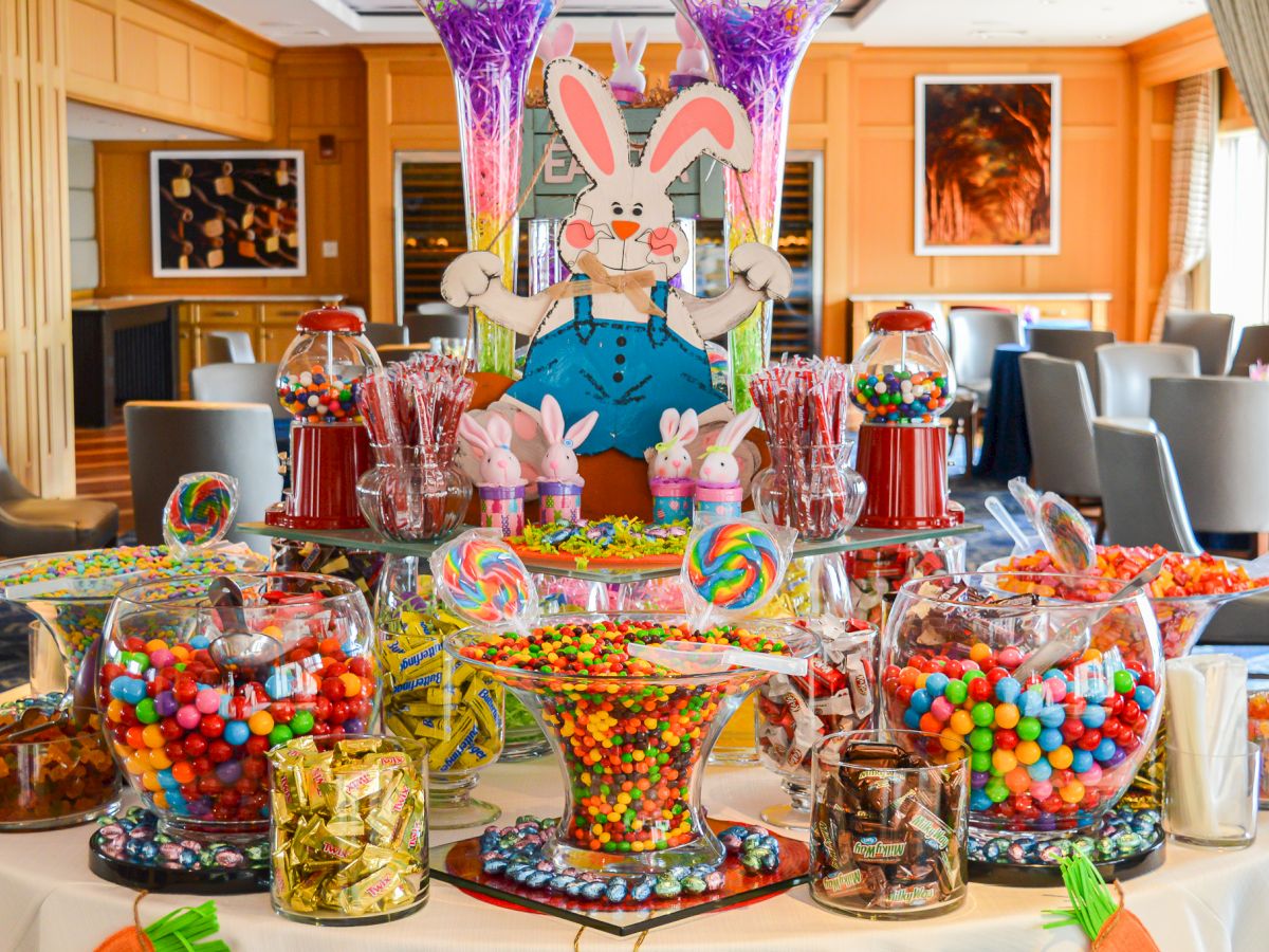 A colorful candy buffet with assorted sweets in jars and bowls, featuring a cartoon bunny decoration in the background.